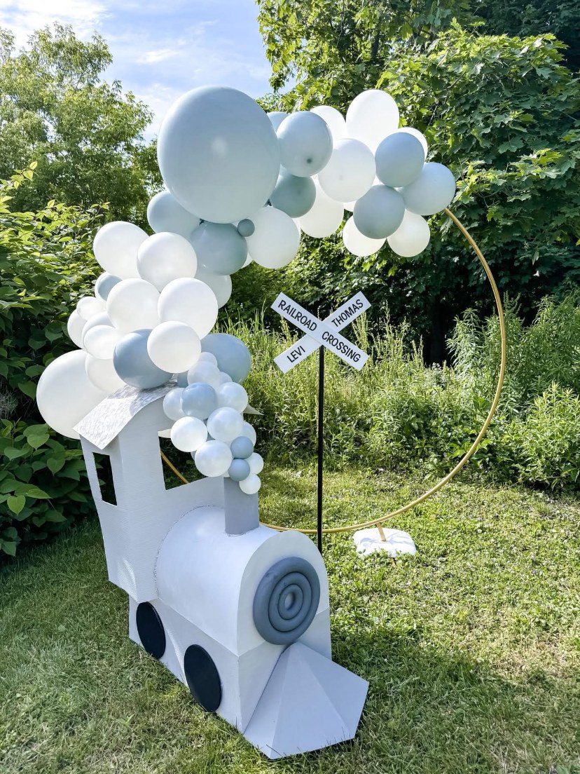 Pale blue and white balloons with a train display outdoors